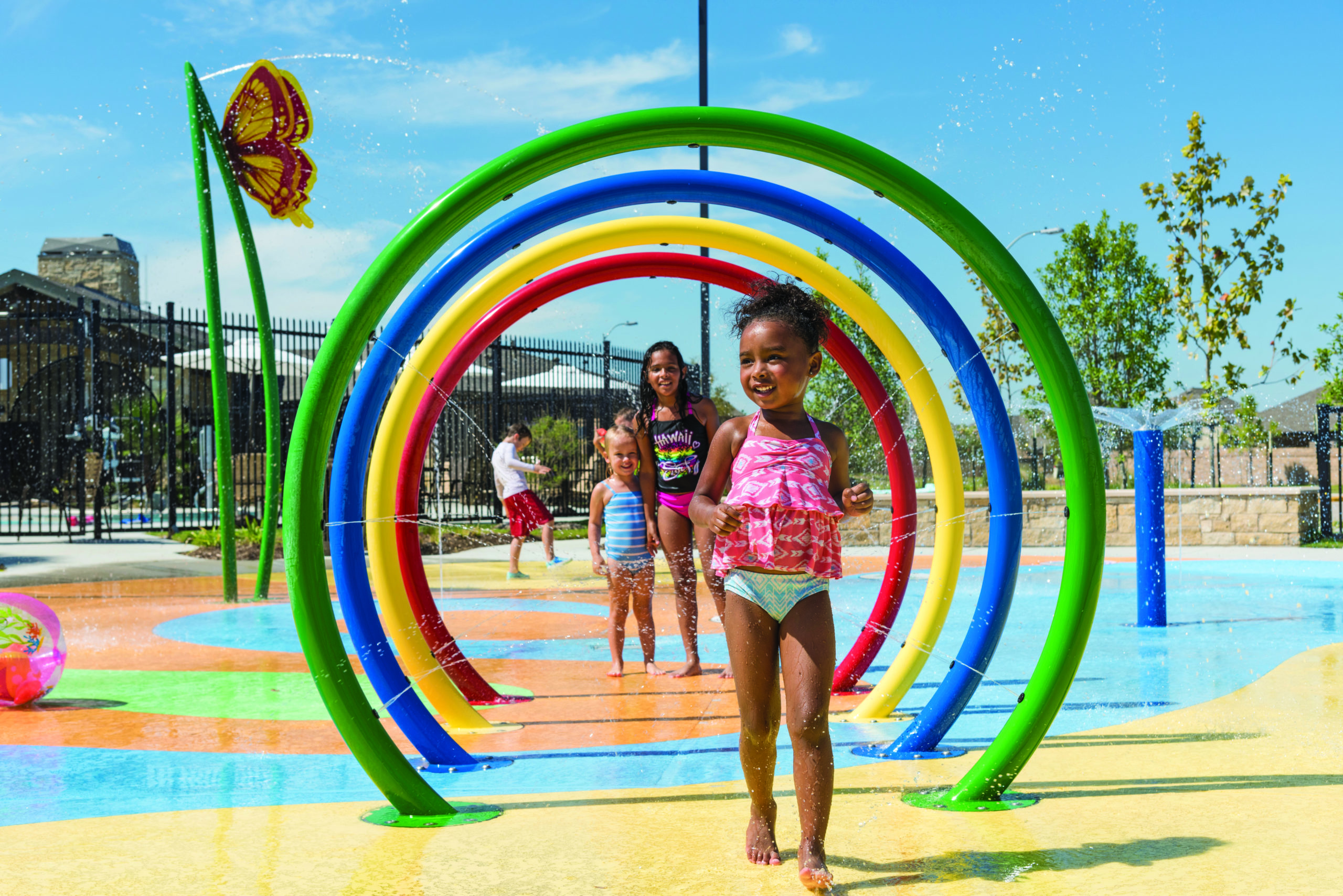 Children run through colorful water arches at a splash pad on a sunny day near Richmond in Fort Bend County.