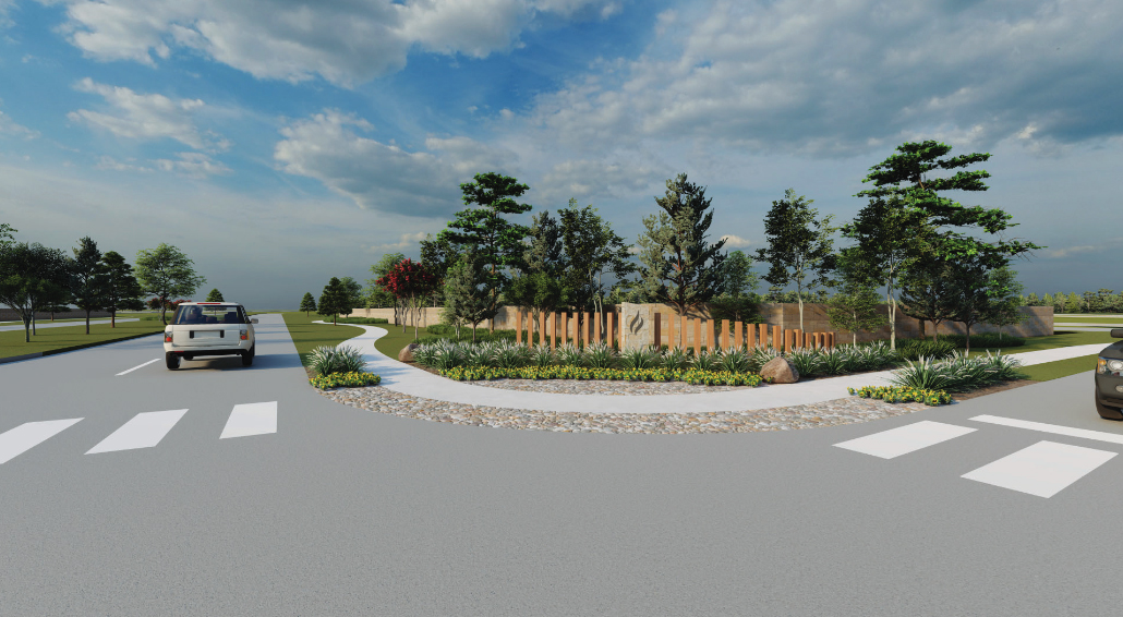 A roundabout with landscaping and a pedestrian crosswalk near Rosenberg. Trees and plants are arranged in the center, bordered by a low stone wall. Two vehicles are approaching the roundabout from different directions. This scenic spot is surrounded by new homes in Fort Bend County.