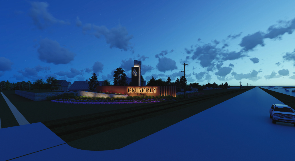 A well-lit entrance sign for Emberly is displayed at dusk. Trees and a garden surround the sign, and a road with a parked car is visible on the right, capturing the serene charm of Fort Bend County near Richmond.