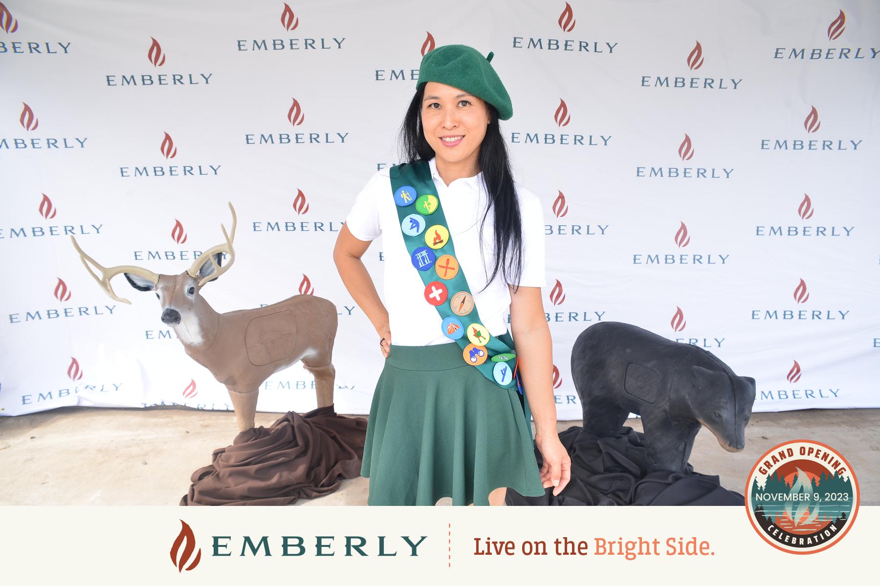 A person in a scout uniform stands in front of a backdrop that reads "EMBERLY," a new homes development near Richmond. Two deer models are positioned behind them, with the text "EMBERLY" and "Live on the Bright Side" visible at the bottom.