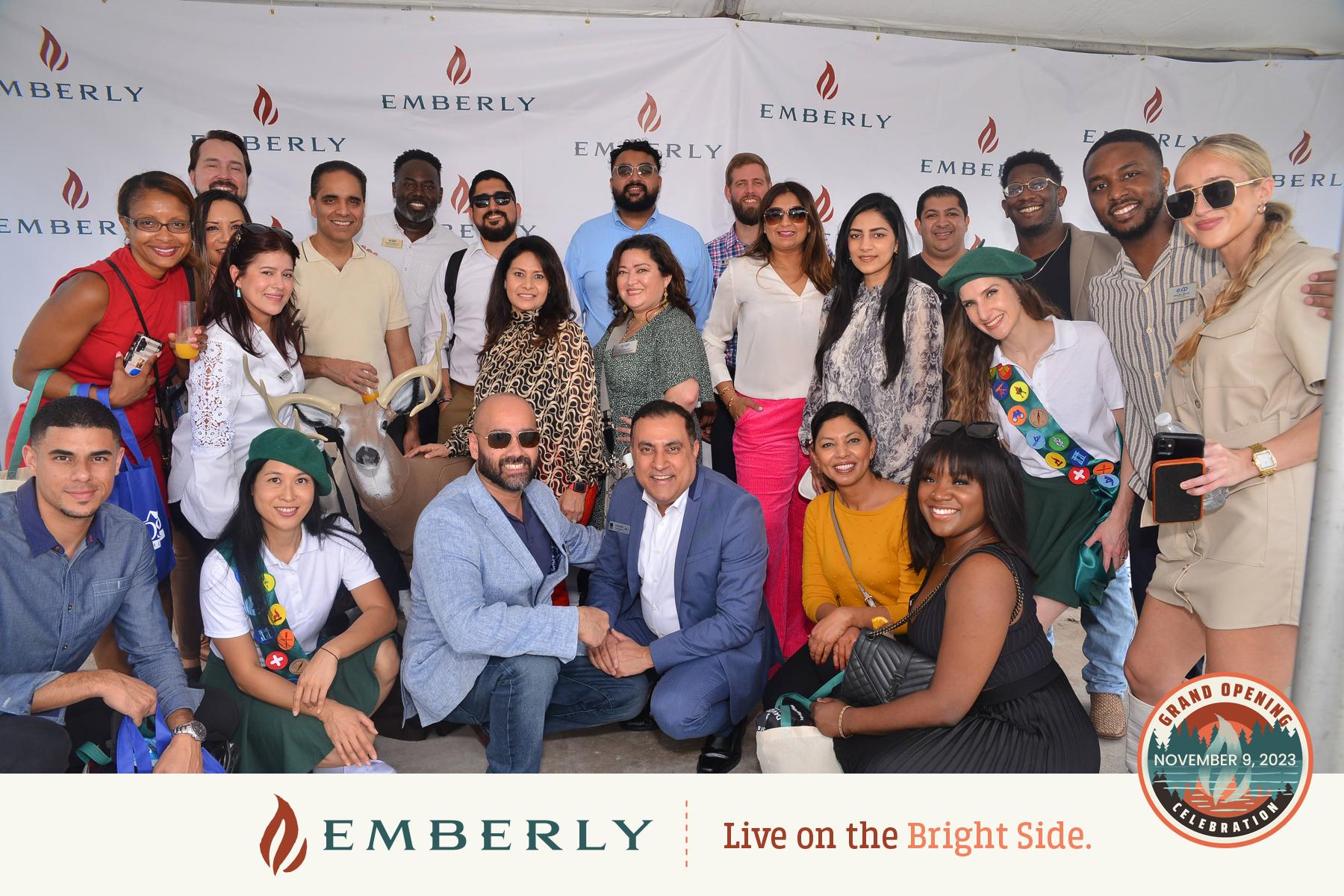 A diverse group of people pose together at the Emberly Grand Opening event on November 9, 2023. They are standing in front of a branded backdrop with the slogan "Live on the Bright Side," celebrating this new master planned community near Rosenberg in Fort Bend County.