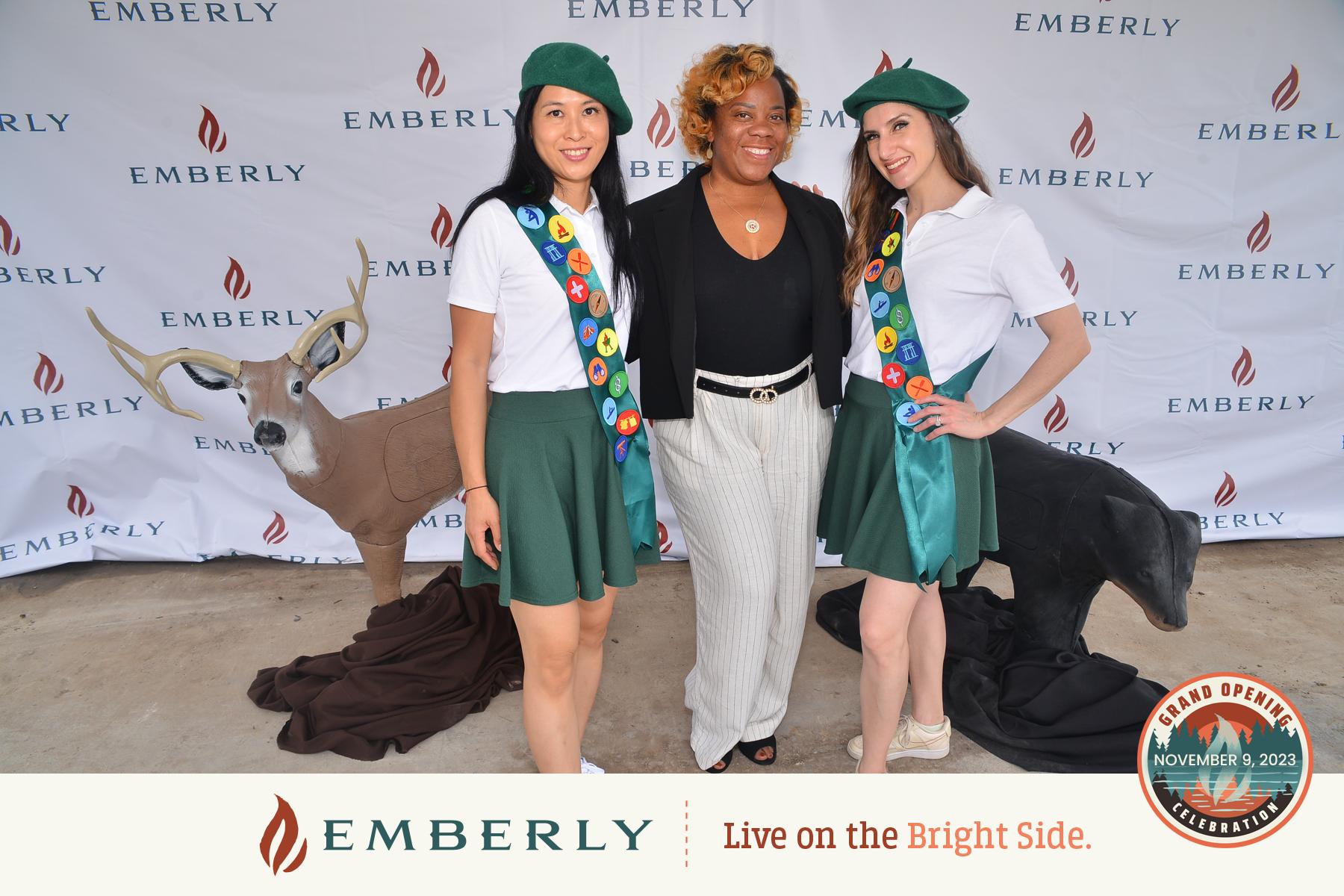 Three people stand in front of an Emberly-branded backdrop. Two wear green berets and sashes, and the third wears a black top and striped pants. Two life-sized animal sculptures are in the background, creating a picturesque scene near Richmond in Fort Bend County.