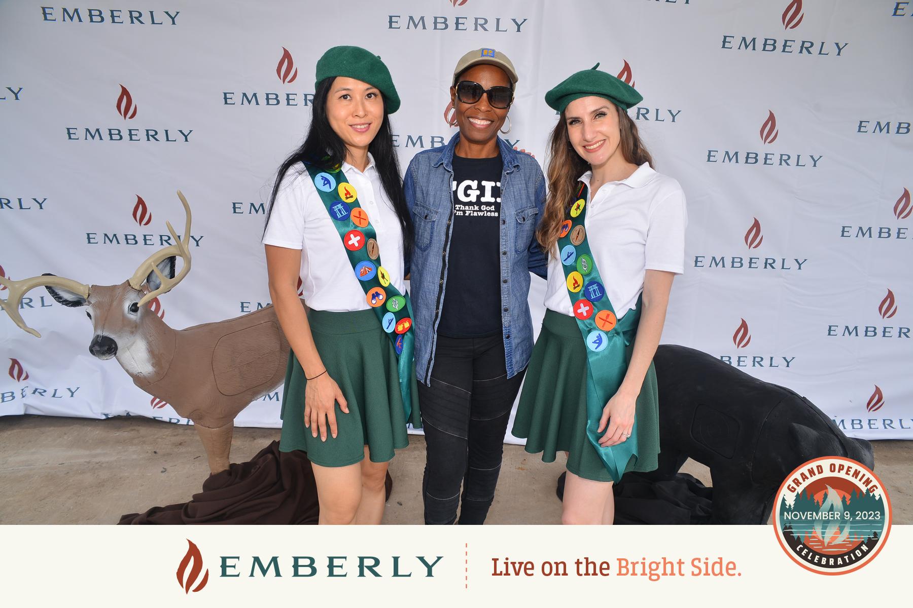 Three people pose for a photo in front of an Emberly-branded backdrop, two wearing scout uniforms with badges. A deer figure is seen in the background, reflecting the natural beauty of Fort Bend County