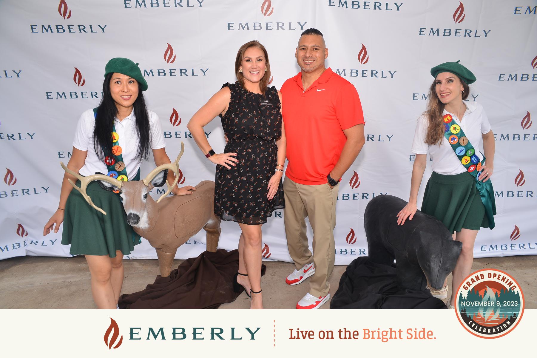 Four people posing together in front of an Emberly banner, with two dressed as scouts and two animals, a deer and a dog, at their sides. The logo for Emberly new homes near Richmond and the event date are displayed on the lower third of the image.