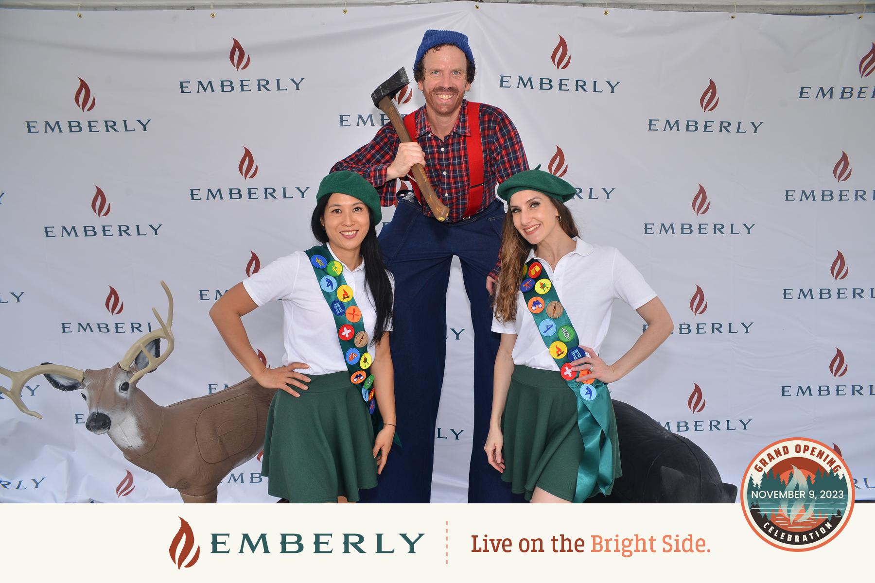 Three individuals pose in front of an Emberly backdrop near Richmond; one on stilts dressed as a lumberjack, and two in scout uniforms standing beside taxidermy deer. Event date: November 3, 2023. Discover new homes with Emberly!