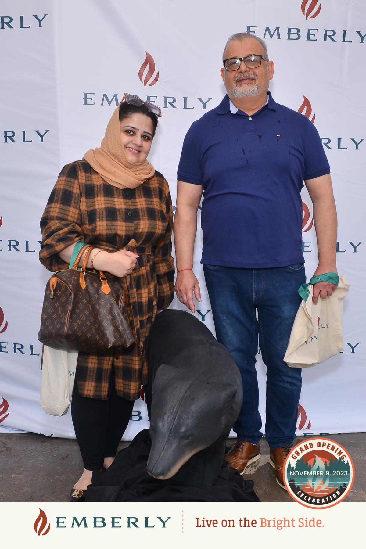 A man and a woman stand near Rosenberg in front of an Emberly-branded backdrop, holding Emberly tote bags, and posing next to a black statue of a dolphin, capturing the essence of the master planned community.