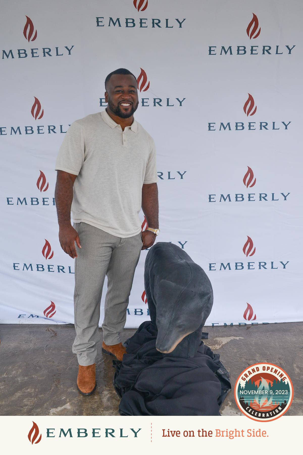 A man stands smiling in front of a backdrop with "Emberly" logos, near Richmond in Fort Bend County. A covered object is in front of him. The text at the bottom reads, "Emberly, Live on the Bright Side," with a "Grand Opening November 9, 2023" badge.