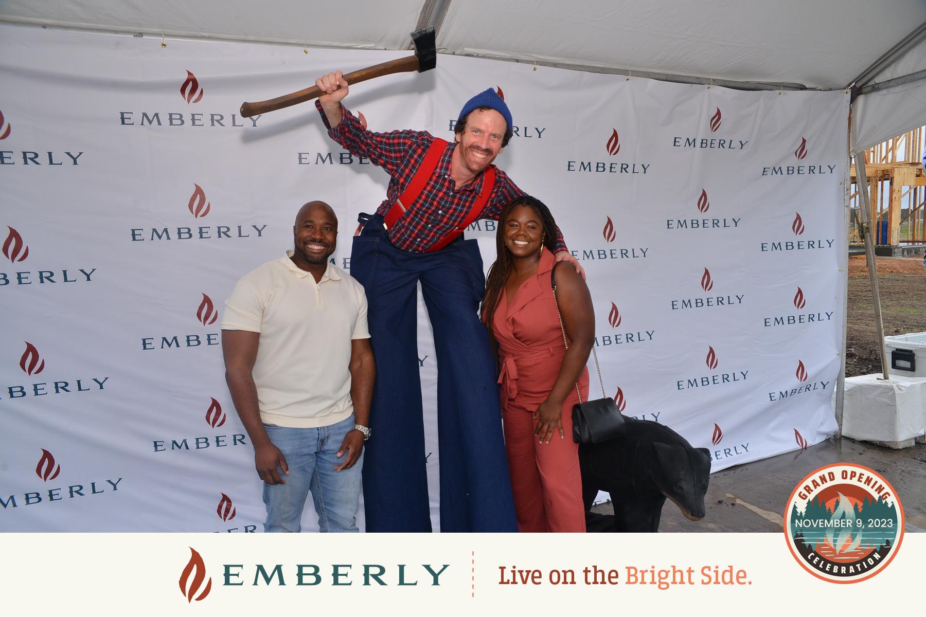 Three people posing for a photo under a tent with an Emberly branded backdrop. One person, dressed as a lumberjack on stilts, towers over two others who are standing and smiling. This vibrant scene showcases the spirit of our master planned community in Fort Bend County.