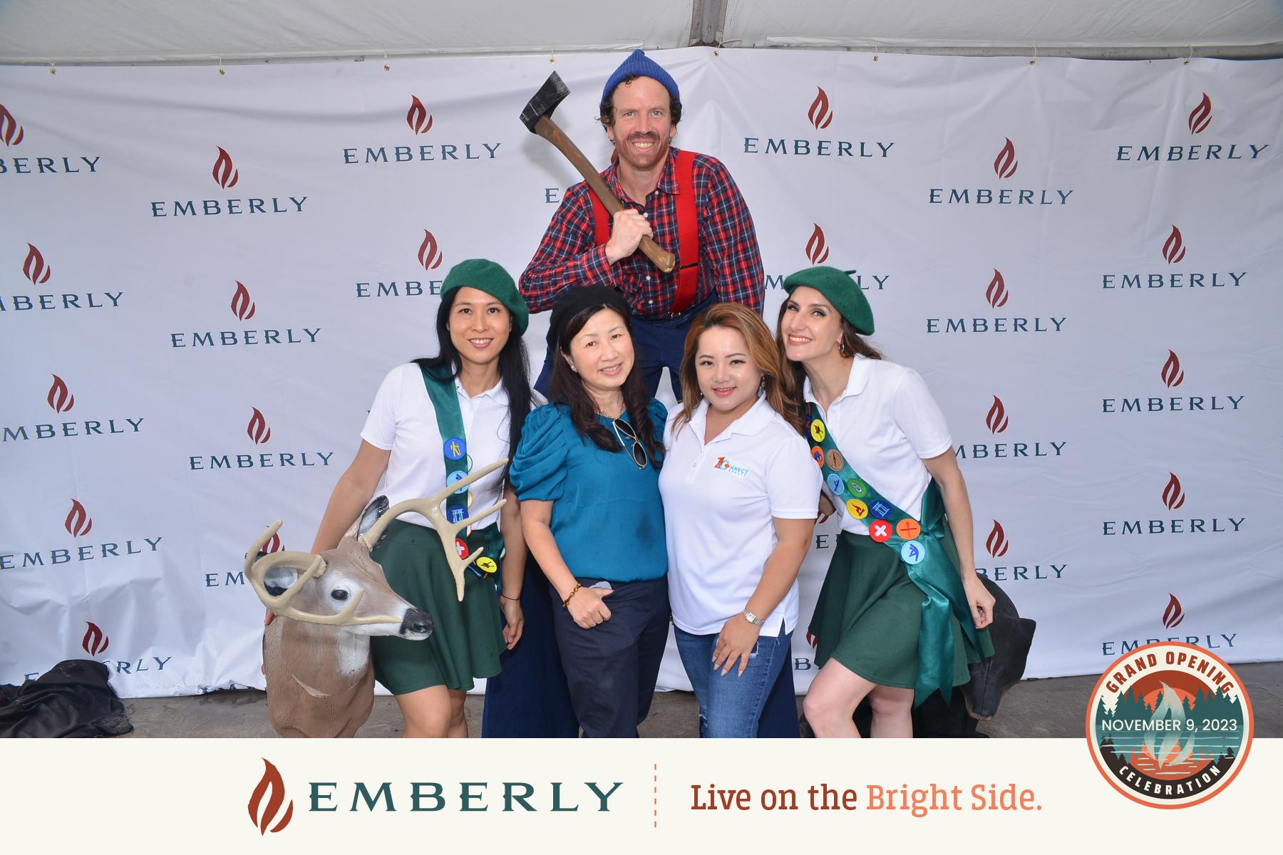 Five people pose together in front of an Emberly-branded backdrop near Richmond. The man at the back is holding an axe and wearing a checkered shirt. Four women, two in scout uniforms, stand at the front, one with a deer prop.