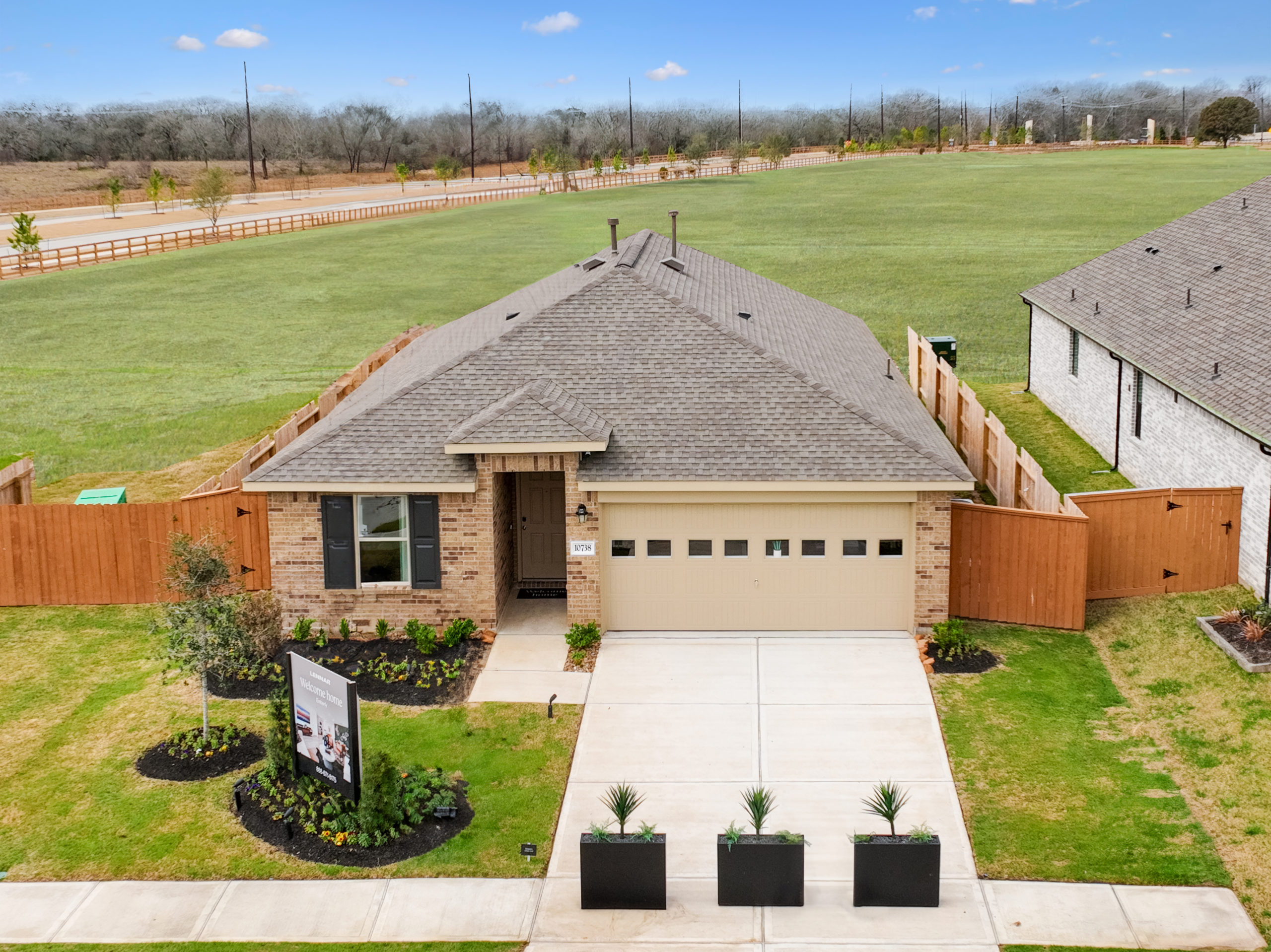 Located in the master planned community of Emberly, this single-story house features a two-car garage, front yard landscaping, and a wooden fence. Nestled in Fort Bend County, it offers serene views of large green fields in the background.