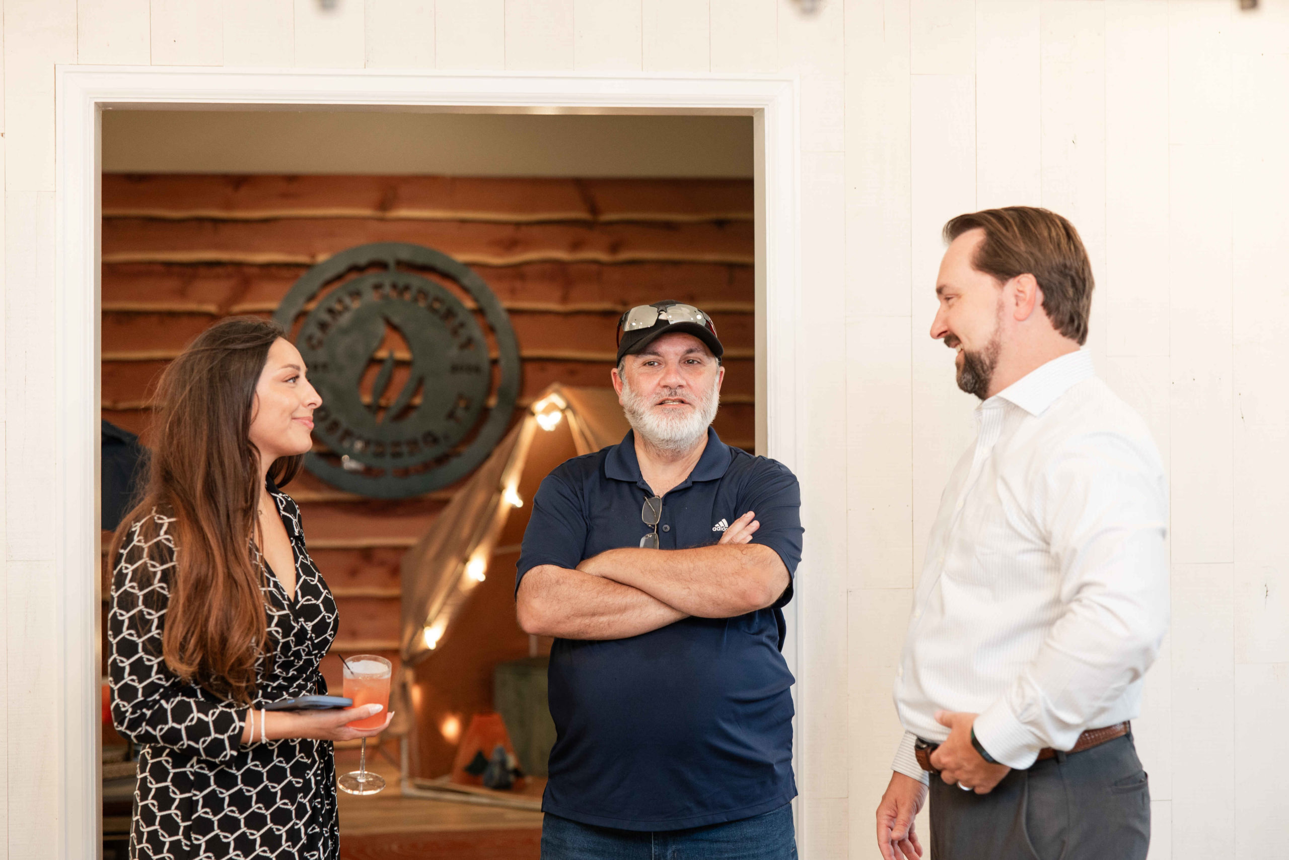 Three people are standing and talking in an indoor space at the Grand Opening Event. Two men and one woman, one man has arms crossed, another is in a shirt and tie, and the woman is holding a glass jar.