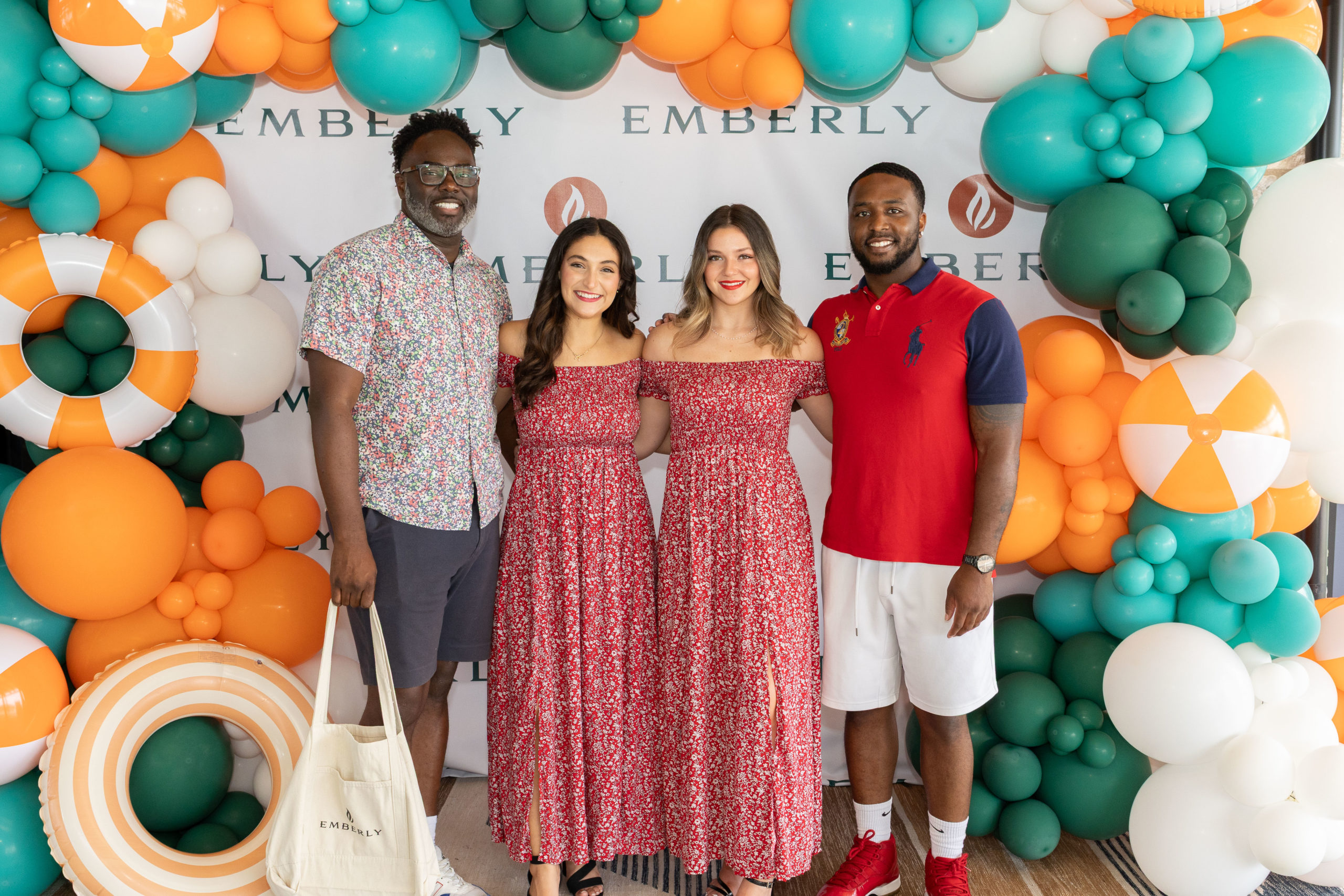 Four people stand in front of a colorful balloon backdrop with "Emberly" branding at the Haven Amenity Village Grand Opening; two women in matching red dresses are in the center, flanked by two men in casual attire.