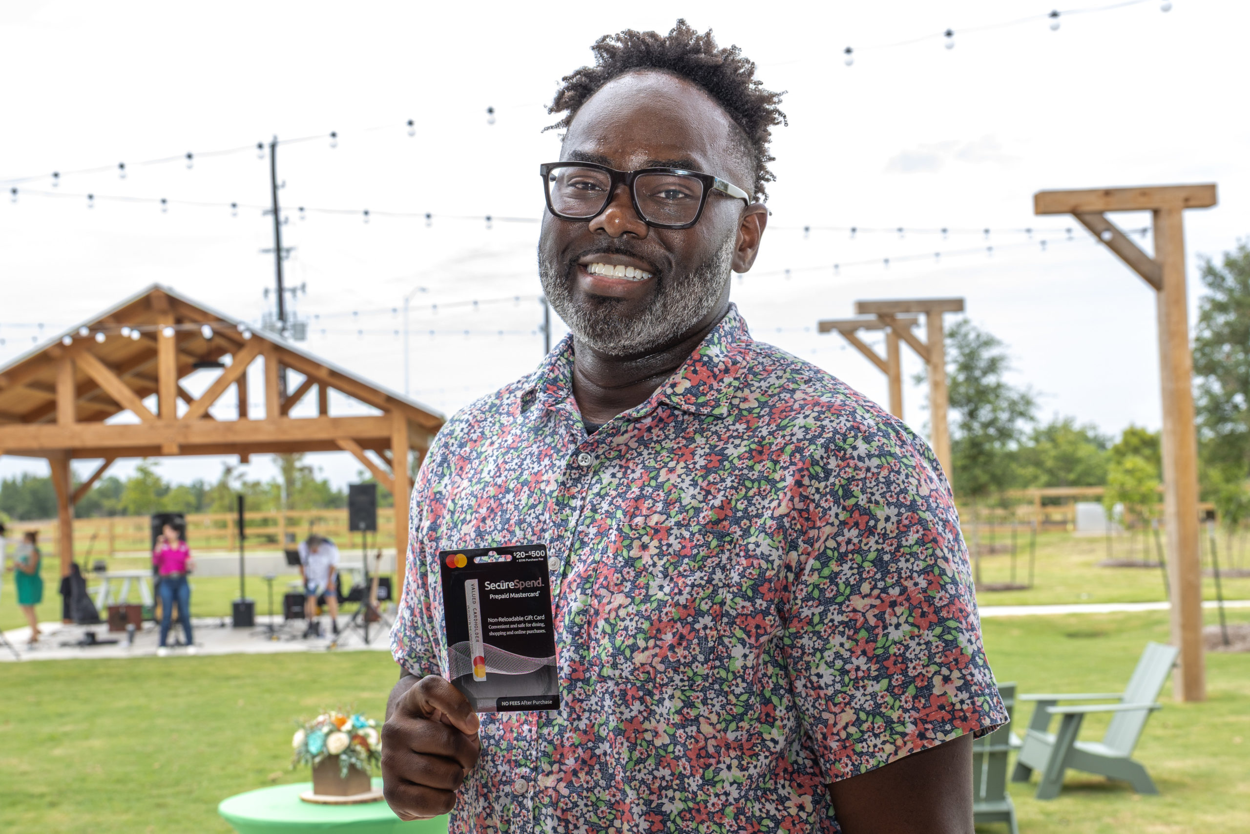 A man wearing glasses and a floral shirt stands outdoors, smiling and holding a pack of Scott