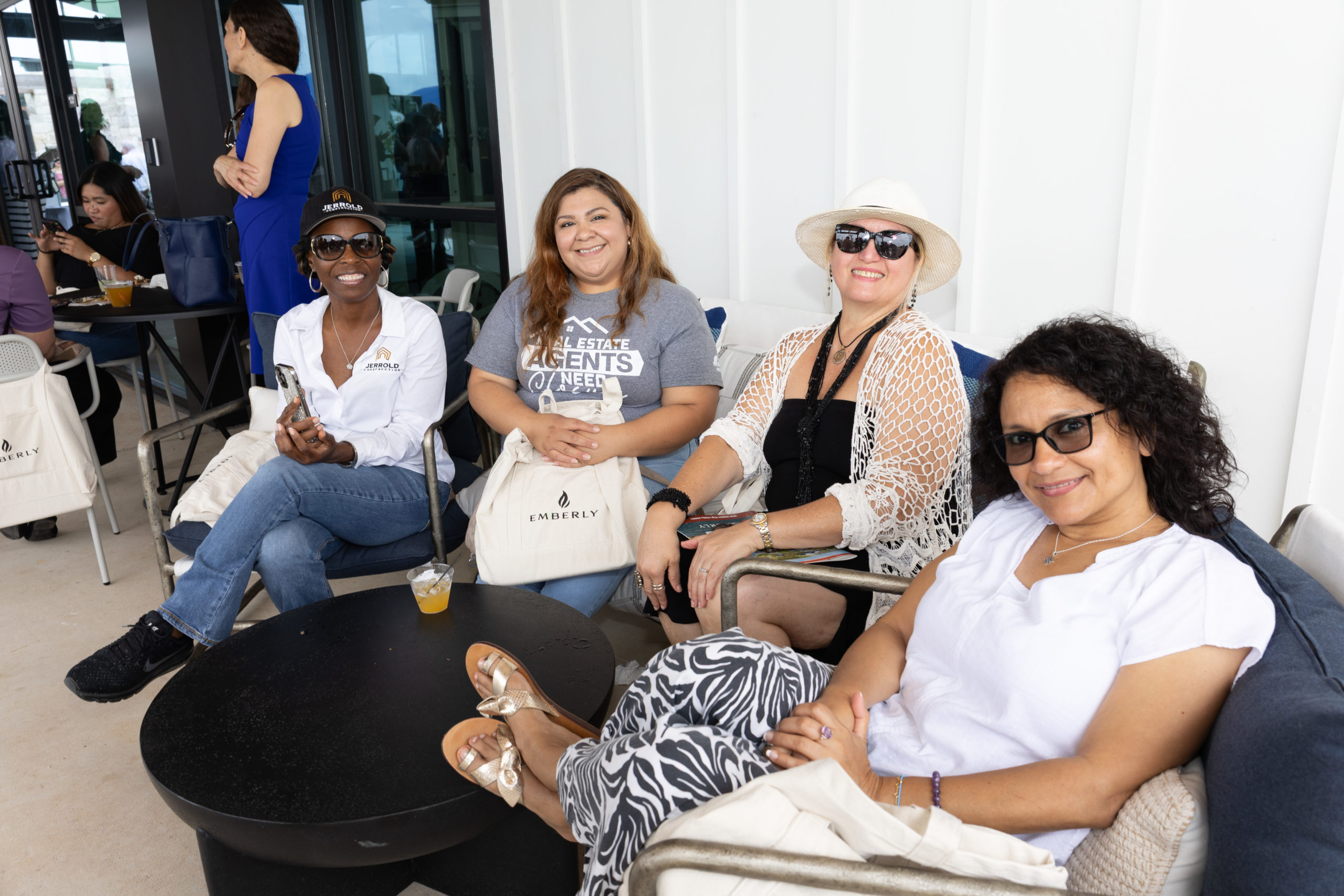 Four women sitting together outdoors at the Haven Amenity Village Grand Opening, smiling at the camera. They are casually dressed and appear to be enjoying a lively social event.