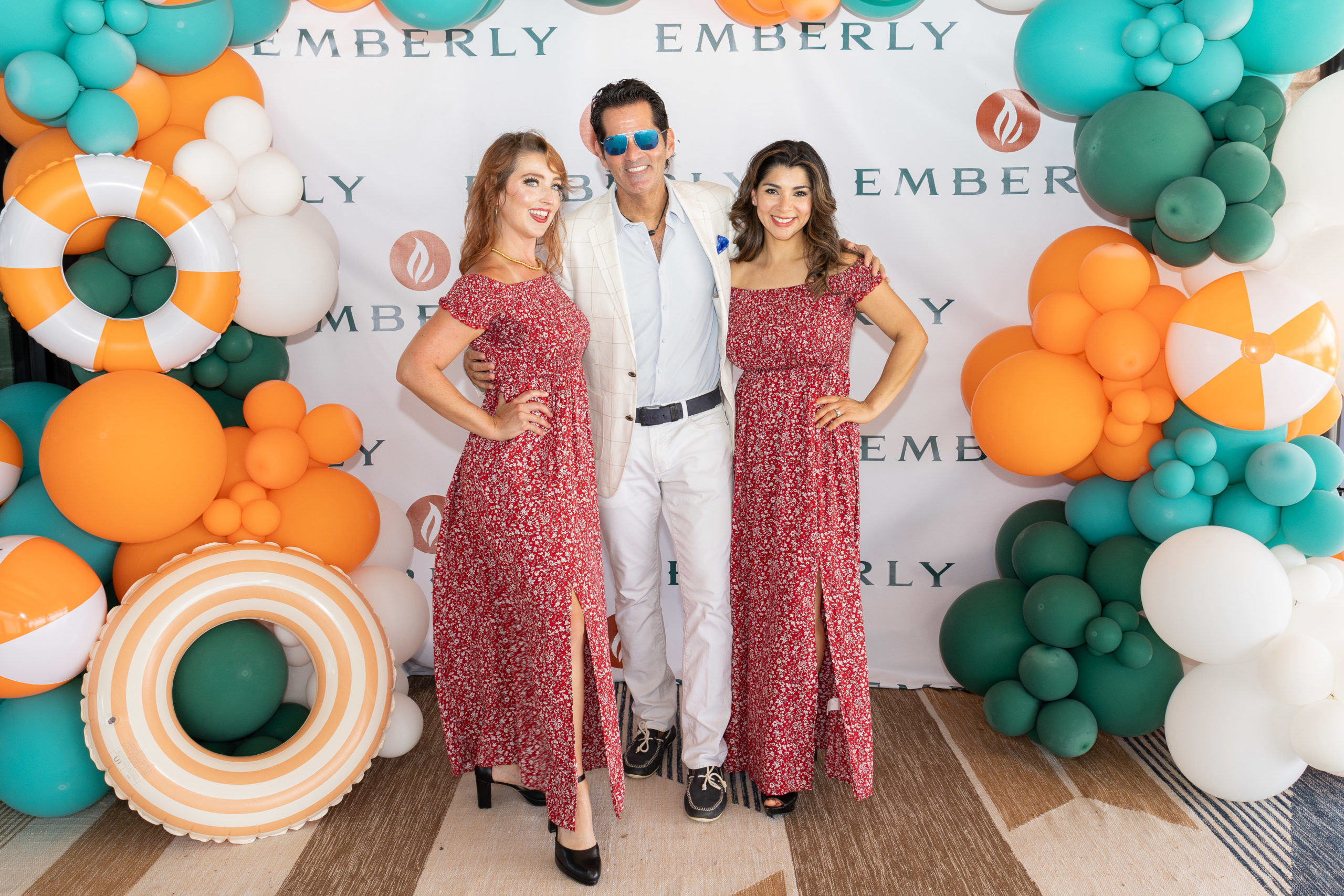 Three people pose in front of an Emberly backdrop at the Grand Opening of Haven Amenity Village, flanked by orange, green, and white balloon decorations, including life buoys and beach balls.
