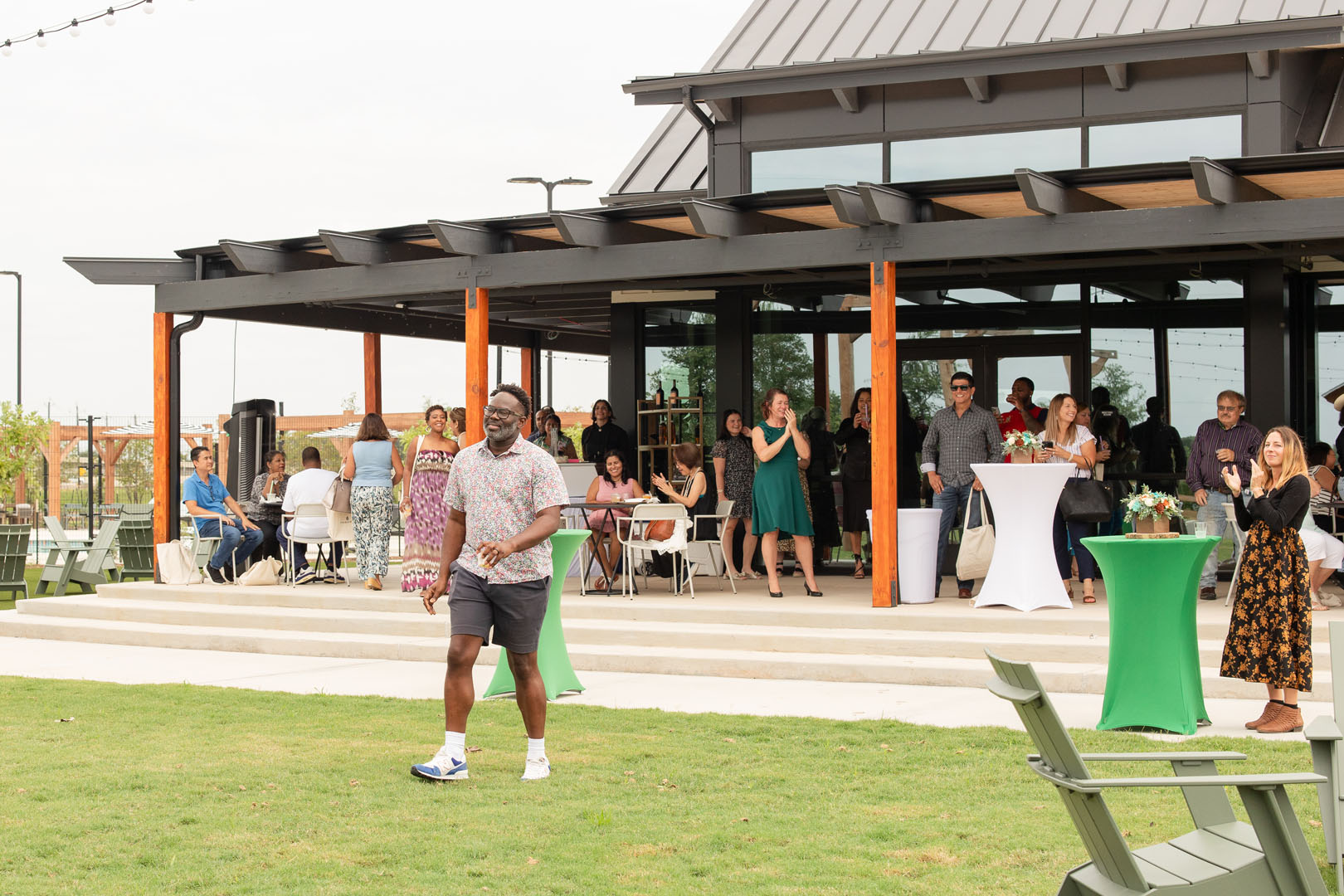 Guests mingle outside a modern building at Haven Amenity Village’s Grand Opening, some relaxing on the patio while others stand around cocktail tables set on the lush grassy lawn.
