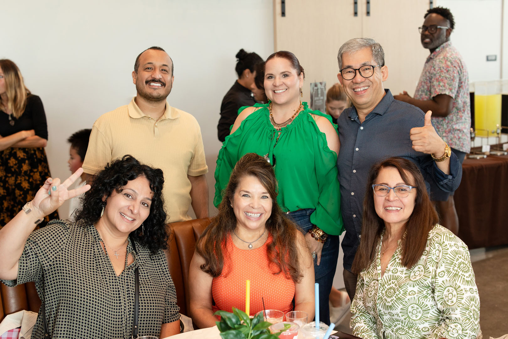 A group of six adults poses and smiles for a photo around a table at the Haven Amenity Village Grand Opening, enjoying the casual indoor gathering.