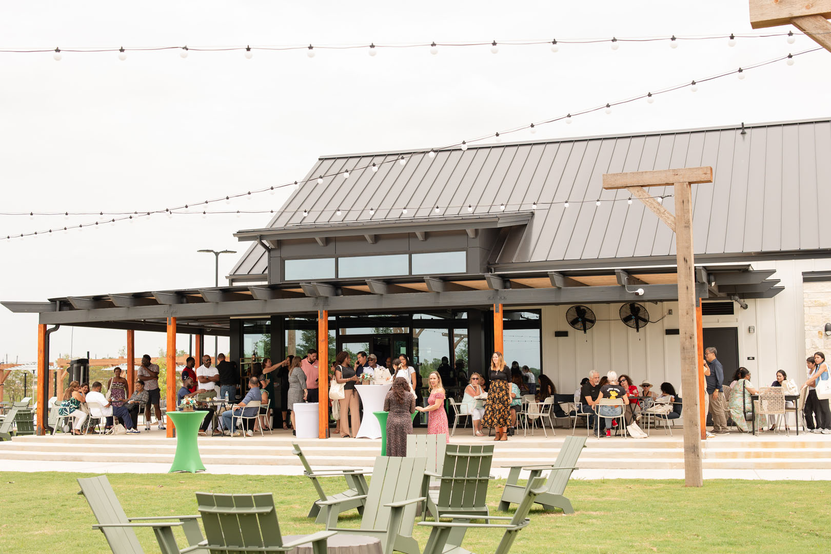 Guests celebrate the Grand Opening at Haven Amenity Village, dining together on a covered patio beneath glowing string lights, with green lawn chairs set in the foreground.