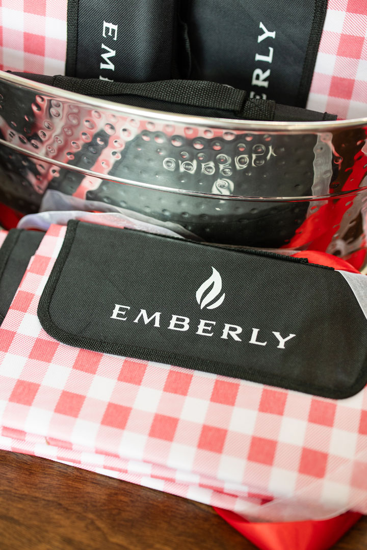 A close-up of a metallic picnic basket filled with red and white checkered picnic blankets labeled "EMBERLY" celebrates the Grand Opening at Haven Amenity Village.