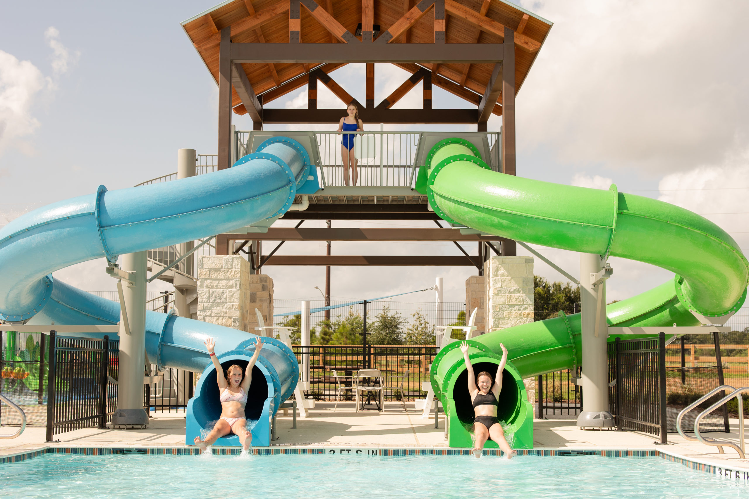 Nestled near Richmond, a spacious park in Fort Bend County features a playground, covered seating areas, lush lawns, and a wooden fenced perimeter. Trees and shrubs are scattered throughout under a partly cloudy sky.