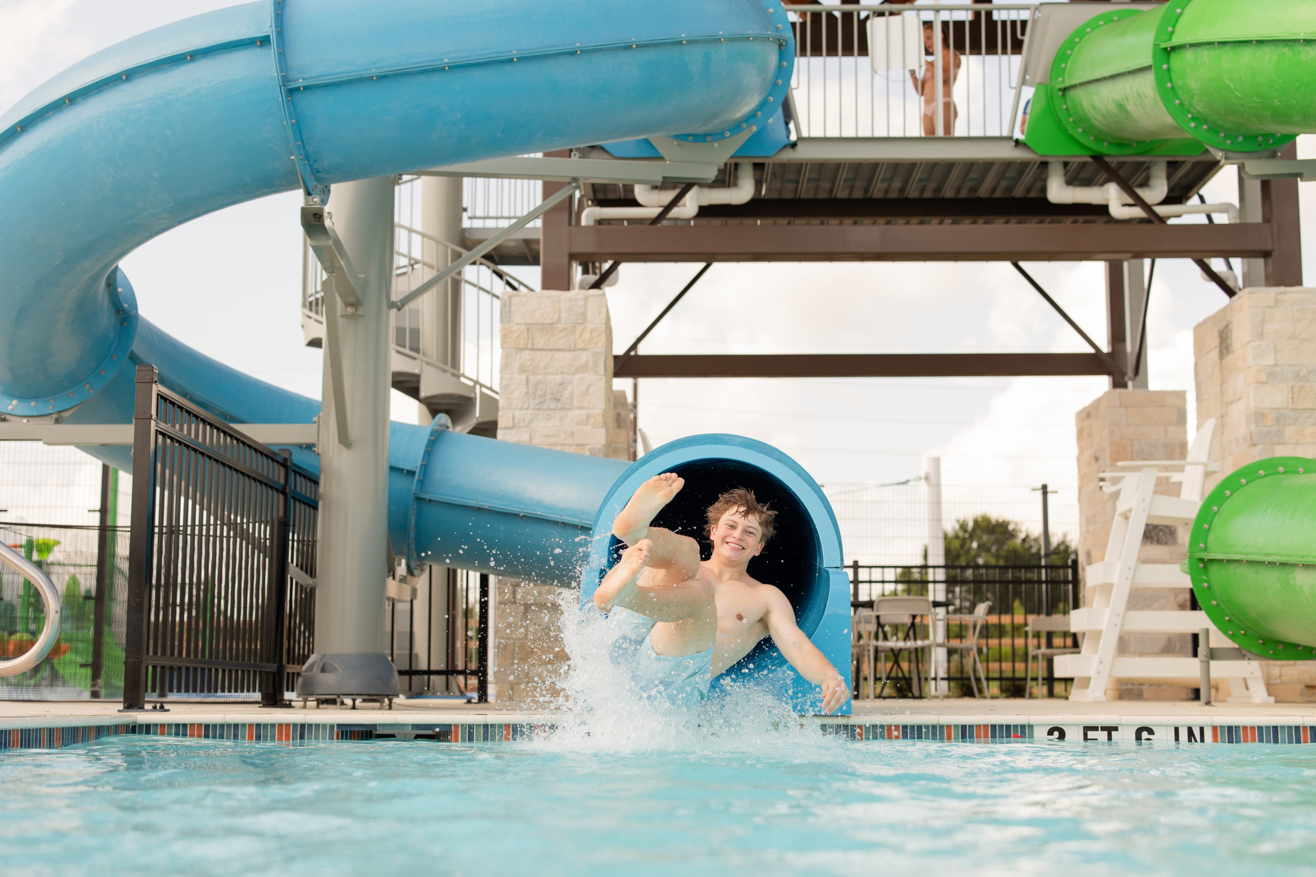 Two children exit a blue water slide into a pool, splashing water at The Haven Amenity Village