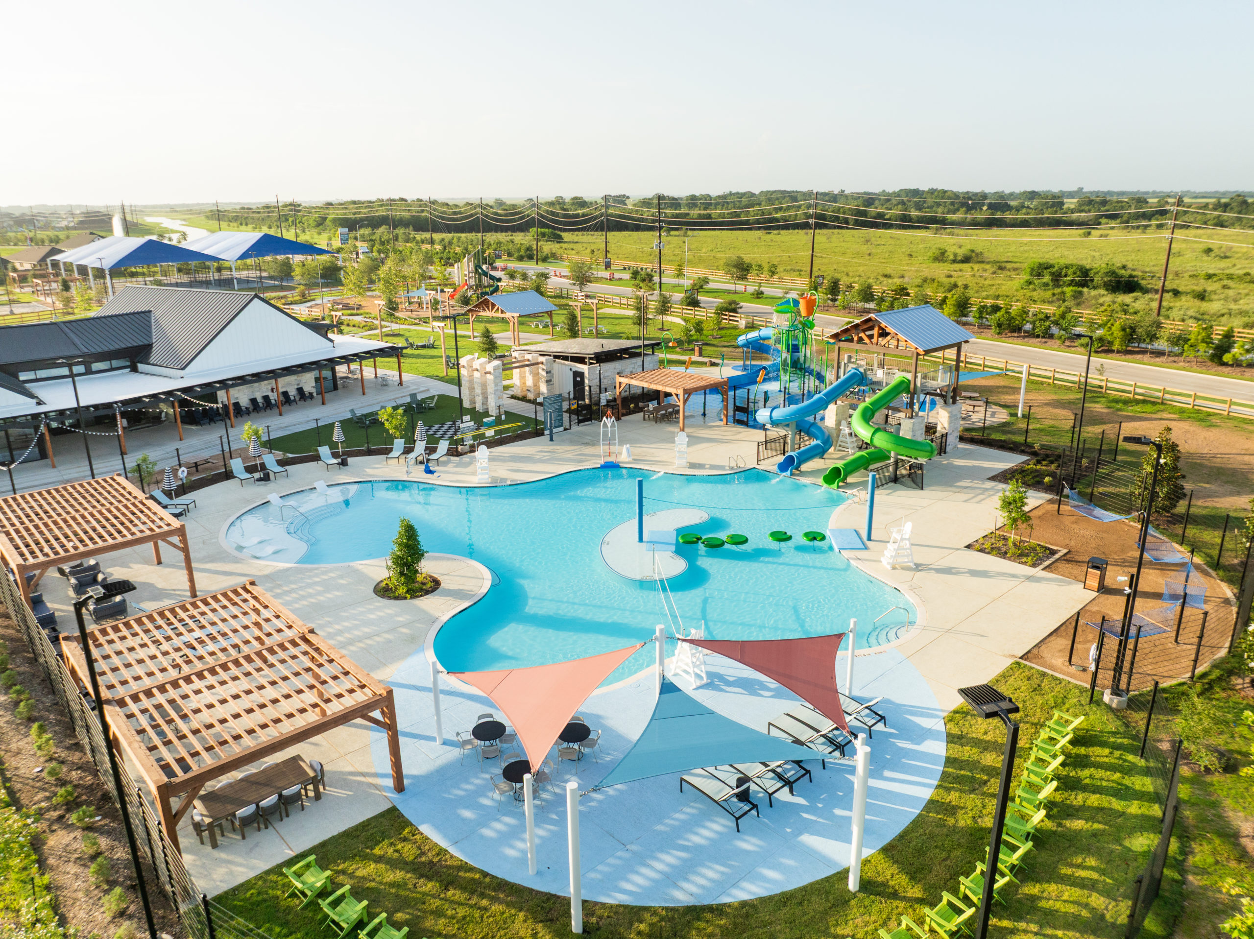 Three children in swimsuits run through colored water archways at the splash pad in Emberly, enjoying a sunny day in Fort Bend County.