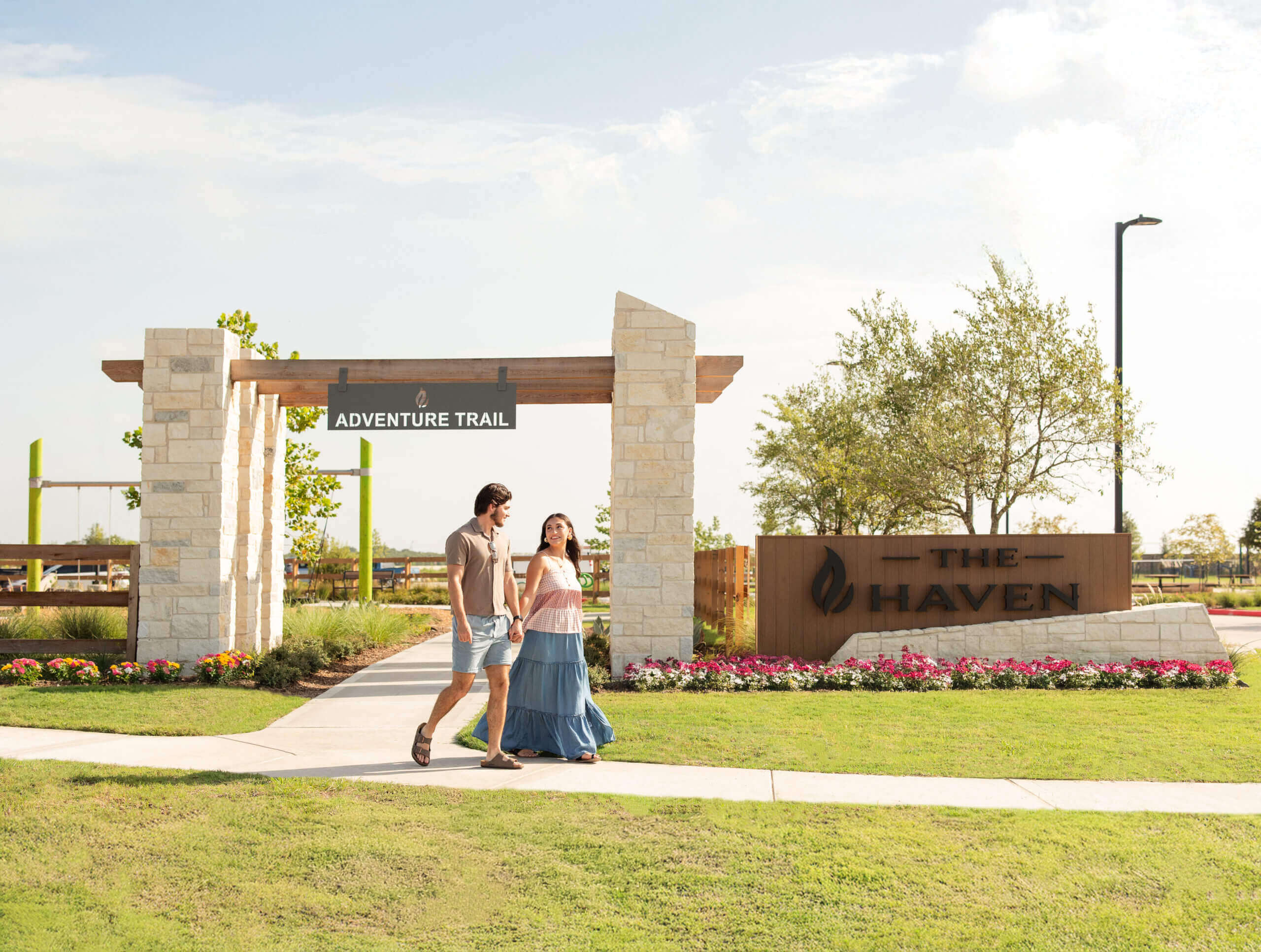 A couple walks past an Adventure Trail arch and The Haven sign in a landscaped area.